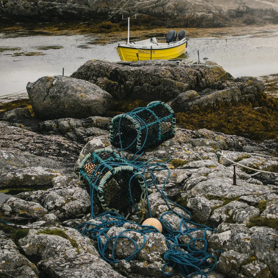 Fishing creels and blue nets on the gneiss shore of Barra, with a yellow boat behind