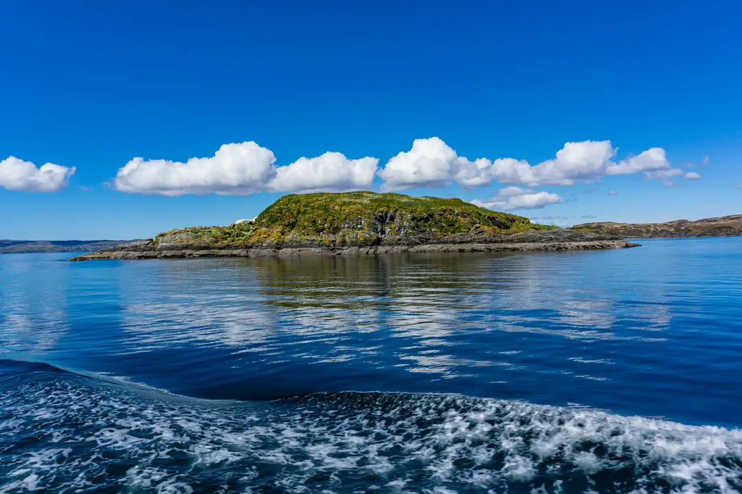 A small green island in deep blue water off the Isle of Eigg