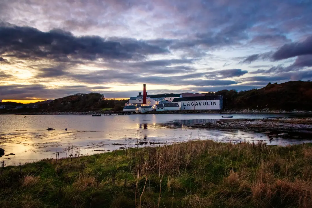 Lagavulin distillery's white warehouses on the shore of Islay at dusk, seen across the bay
