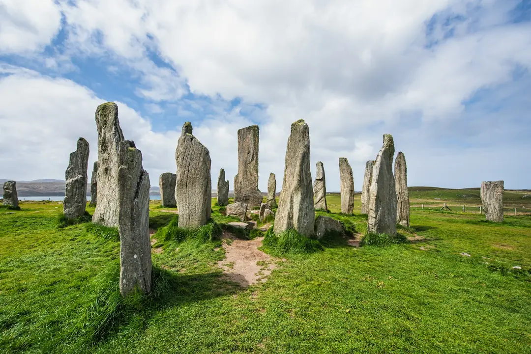 The main Calanais stones on Lewis, lichen-grey slabs standing in green grass with the loch beyond