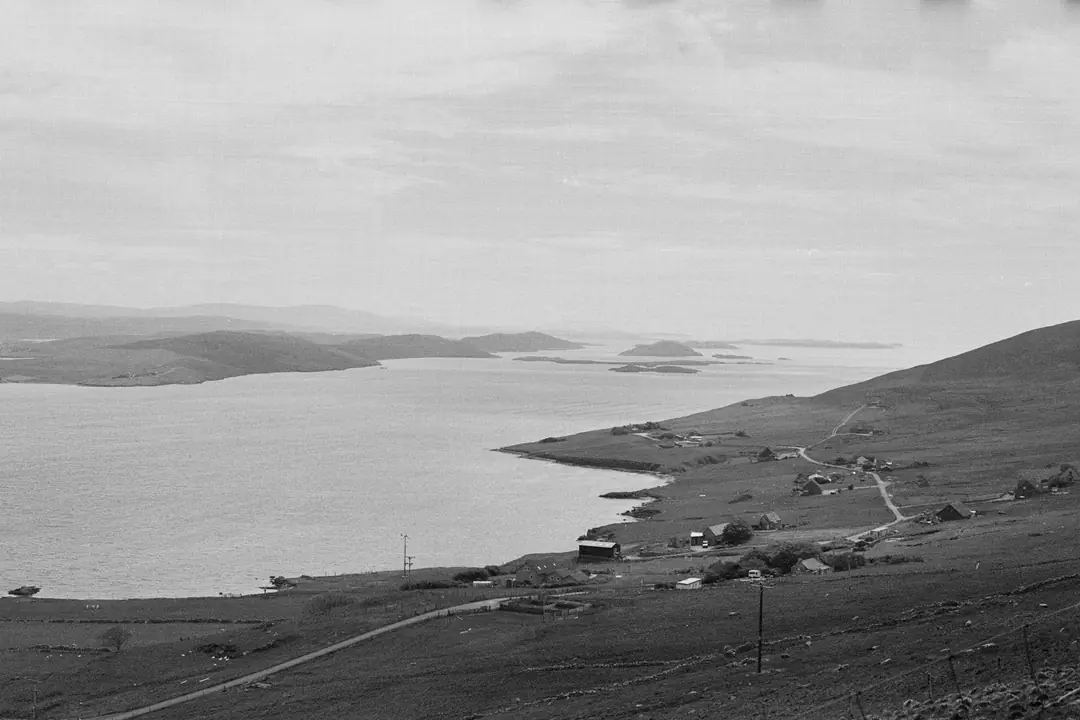 A Shetland settlement on a grassy hillside above a sound, in black and white