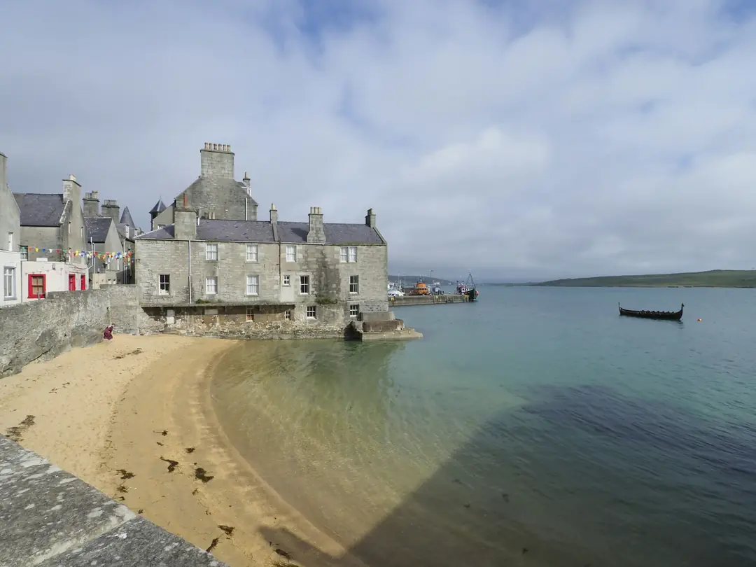 The old stone lodberries of Lerwick standing at the water's edge above a small sandy beach