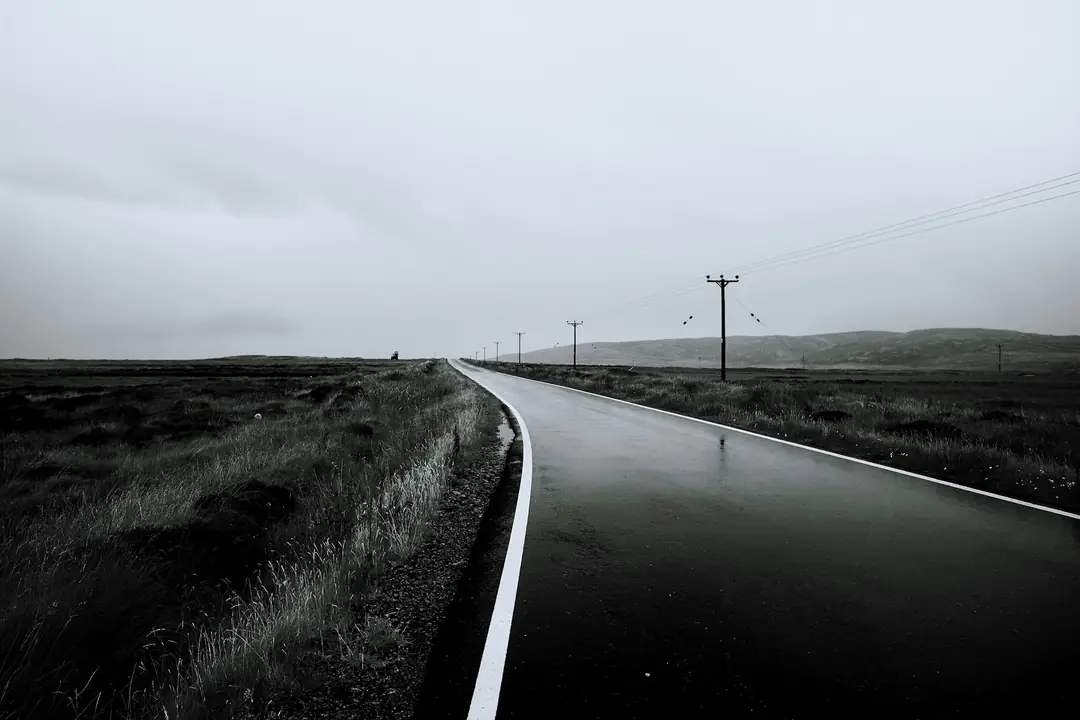 A wet road across the flat peatland of South Uist in black and white, telegraph poles to the horizon